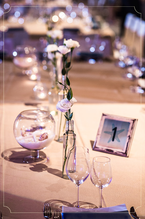 פרחים לבנים וכלי זכוכית שקופים, שילוב מושלם לחתונה בהשראה ימית.