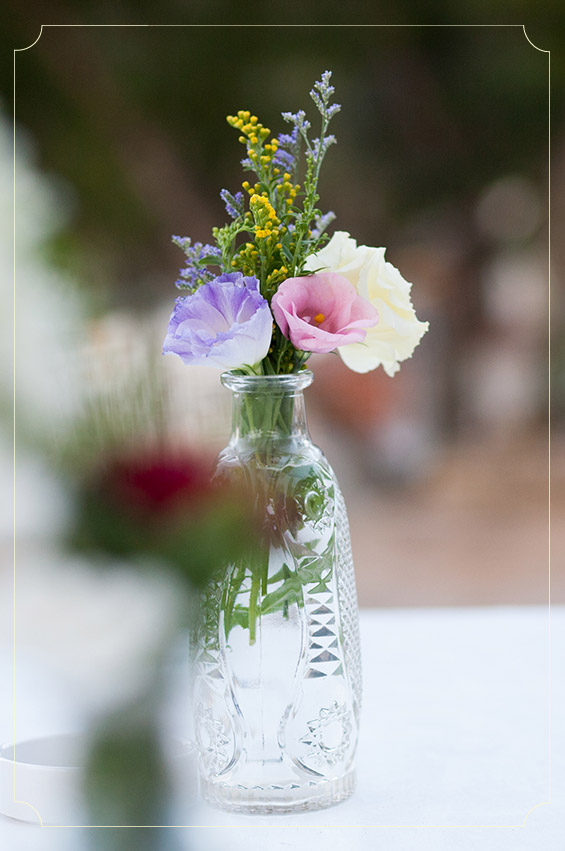 בקבוקי זכוכית שקופים ופרחים צבעוניים כמרכזי שולחנות. צילום: אפרת ציון.
